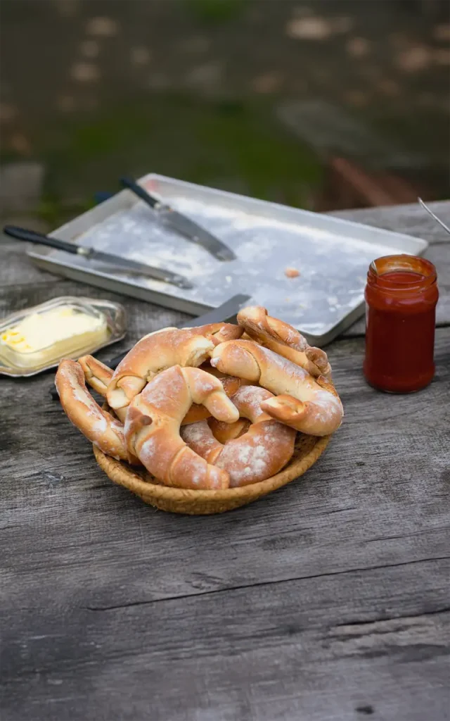 Frische Croissants in einem Korb neben Butter und Marmelade auf einem Holztisch.
