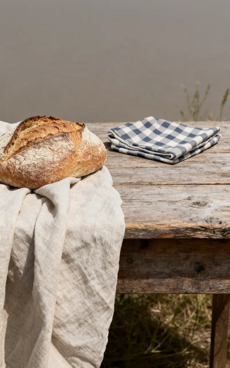 Brot auf einem Tuch auf einer Bank, daneben ein blau weiß kariertes Handtuch